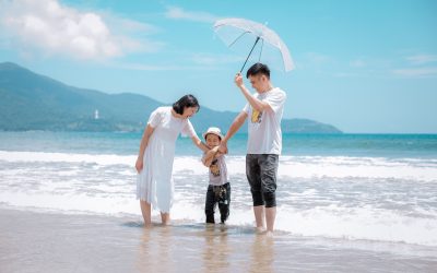 family of three on a beach; father holding an umbrella