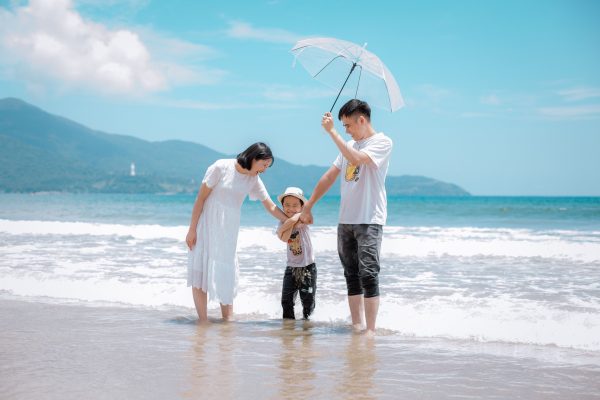 family of three on a beach; father holding an umbrella